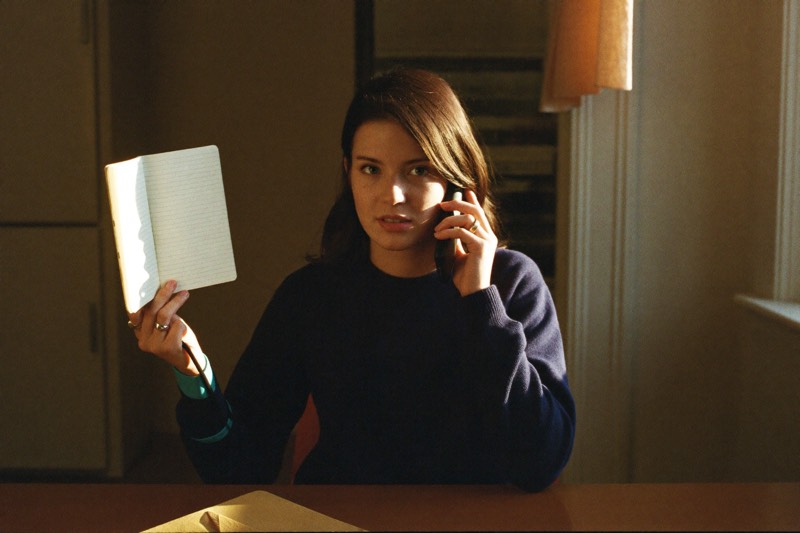 A person on a phone call holds a notebook at a warm kitchen table.
